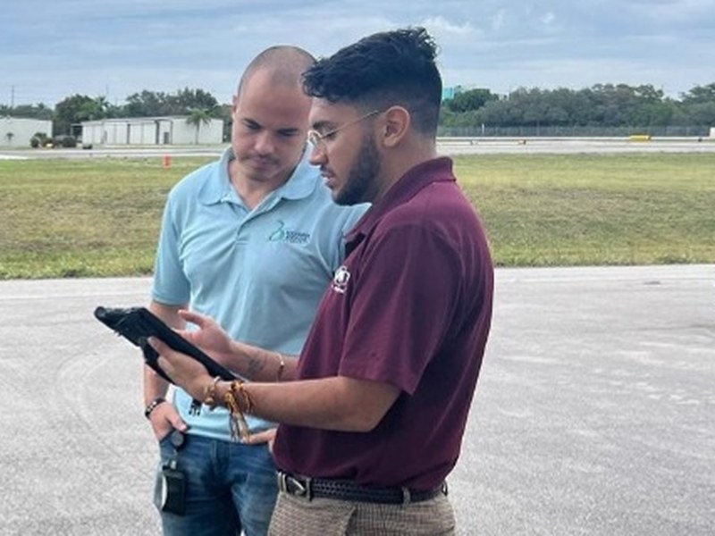 Two Simplify i3 team members reviewing a tablet together during a field training session at an airfield