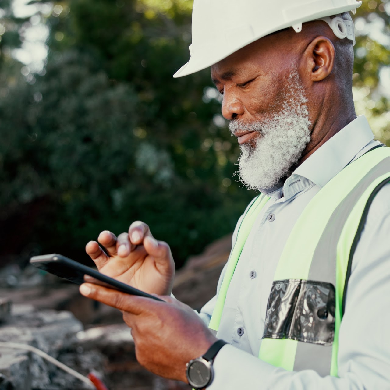 A field technician in a hard hat and safety vest reviewing site data on a tablet